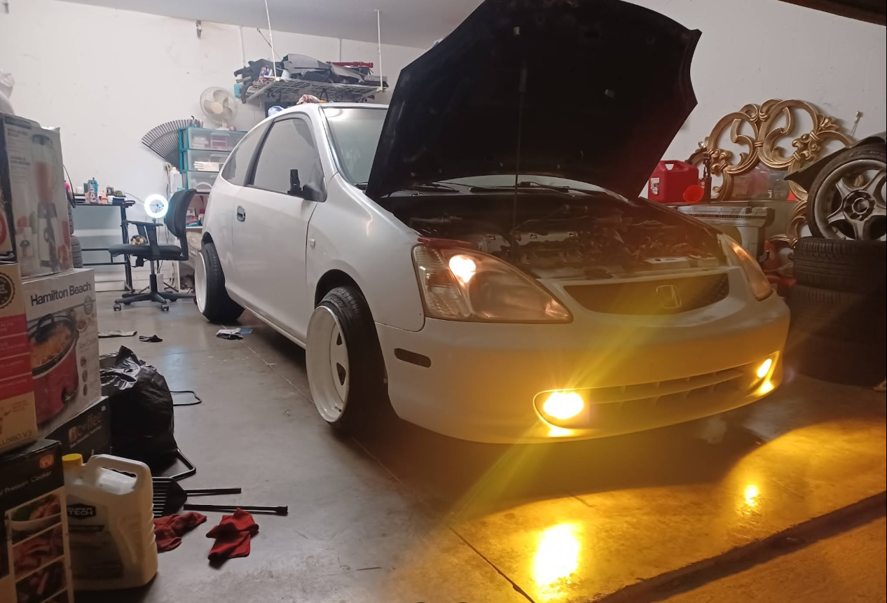 Honda Civic in the shop with hood up, fog lights on, mid-service